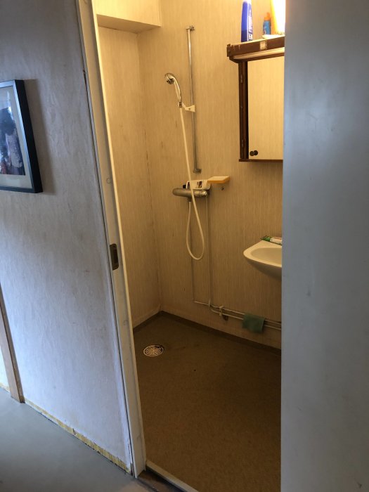 Gammal och sliten duschhörna i ett radhus från 70-talet med beige väggar och tunn duschslang före renovering.