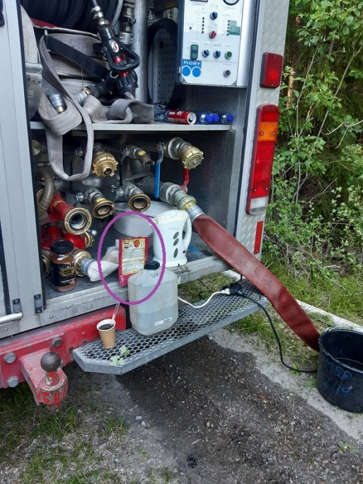 En öppen brandbilslucka som avslöjar slangar och kopplingar med en elgryta och kaffekopp på stegplattformen.