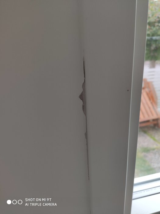 Skadad vägg vid fönsterfoder där färg har lossnat efter att maskeringstejp avlägsnats.