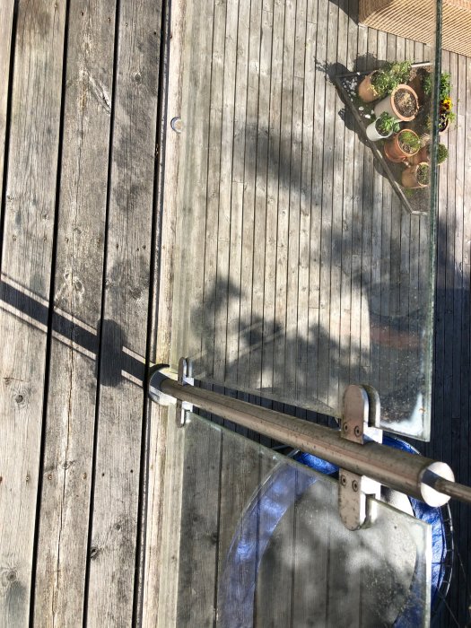 Trätrall med skugga av person och handtag till glasdörr, samt blomkrukor i hörnet.