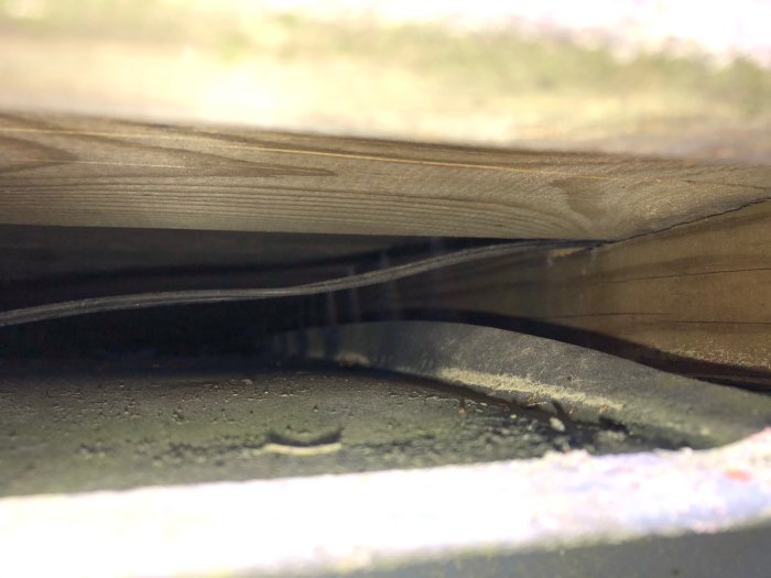 Närbild av ett trägolv med skadade eller upphöjda plankor som visar en glipa.