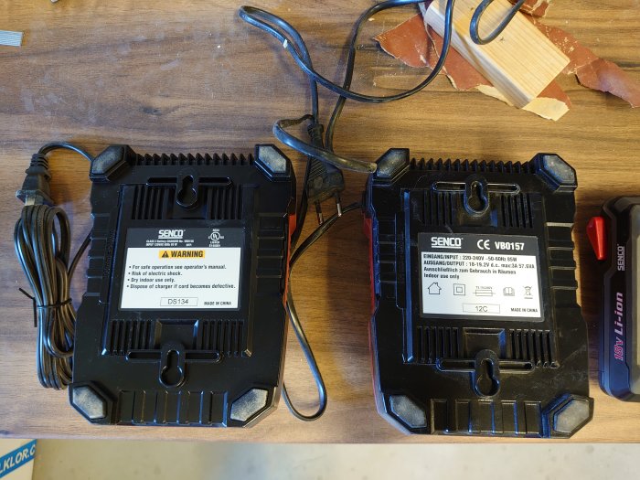 Två identiska batteriladdare på ett arbetsbord, en med en USA-etikett till vänster.