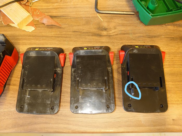 Tre svarta plastbitar på ett arbetsbord, den högra med en blåmarkerad slipad kant.