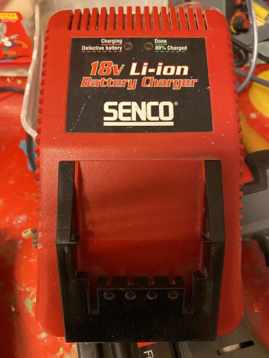 Röd och svart 18V Li-ion batteriladdare från SENCO på arbetsbänk med slipmärken.
