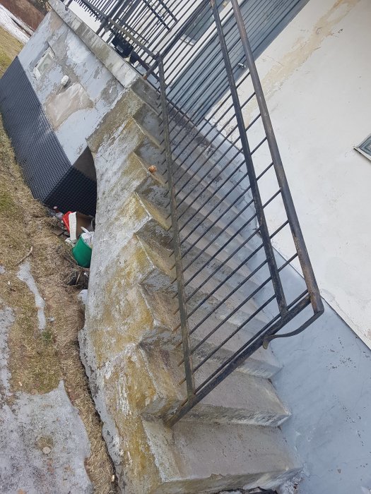 Eftersatt husfasad och trappa med skadad puts och revor, behov av renovering synligt.