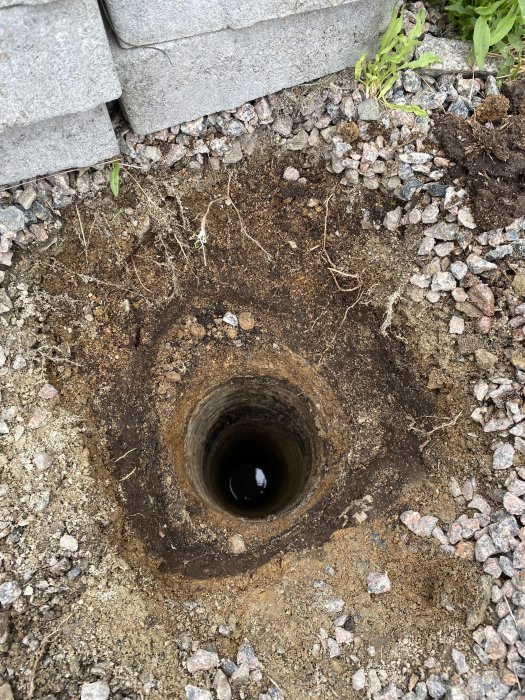 Jordborrhål i marken med synligt grundvatten mindre än 2 meter ner, bredvid gråsten och betongblock.