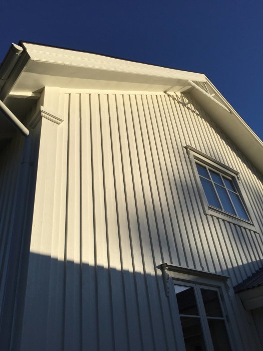 Ny målad fasad av ett hus med liggande vita paneler och fönster i solljus.