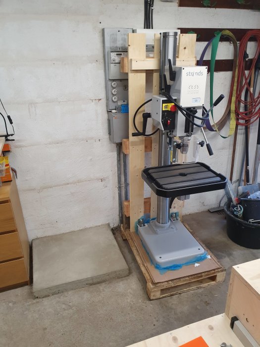 Tung maskin på träpall bredvid en nyligen gjuten betongsula i ett verkstadsutrymme.