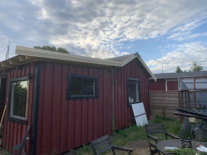 Röd trästuga med nylagda vindskenor på ena sidans tak mot en himmel med moln.