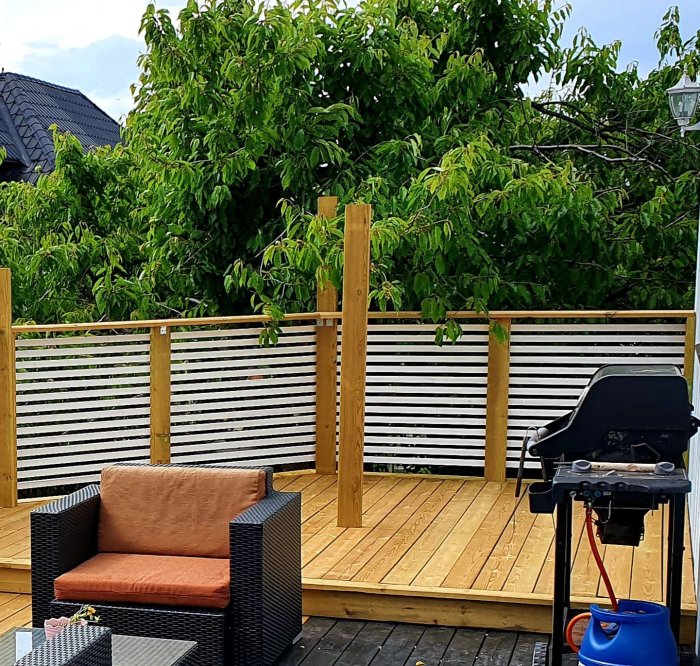 Utemiljö med en nybyggd trädäck och sittmöbler, inklusive grill och vita insynsskydd.