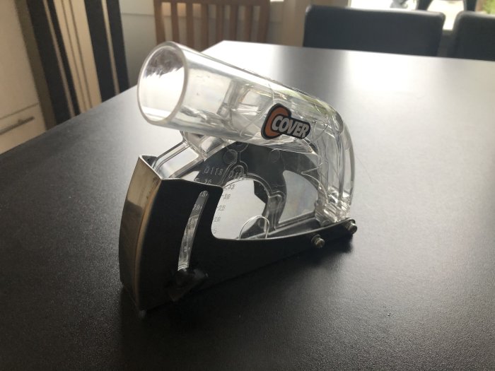 Monteringsfäste med en genomskinlig plastkupa med etikett, troligen en armatur, på ett bord.