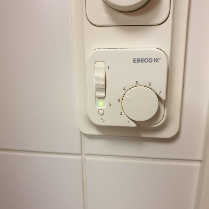 Vit golvvärmetermostat av märket Ebeco på en kakelvägg indikerar en inställning mellan 3 och 4.