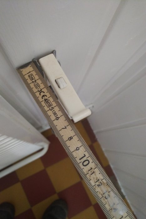 Skadad vit väggkonsol för oljefylld elradiator med ett mätsticka som visar storleken.