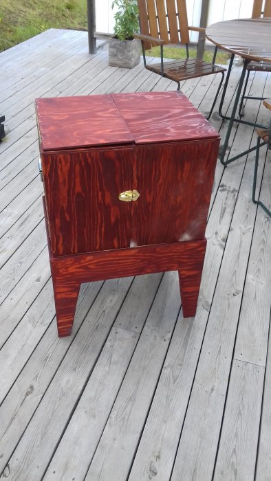 Nybyggd rödfärgad träbyrå med blank yta och gyllene handtag, placerad på en träaltan.