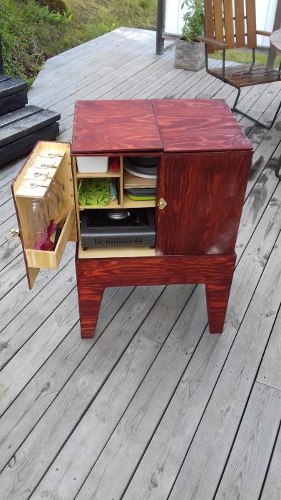 Hemmagjort förvaringsskåp i trä på en träterrass med öppna lådor och innehåll som köksutrustning.