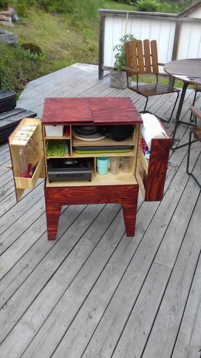 Handgjord förvaringsbänk i trä med öppna fack och rödlackerat lock, stående på utomhusträdäck.