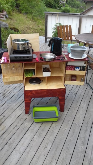 Egetbyggt utekök av trä med köksredskap och kastruller på en altan.