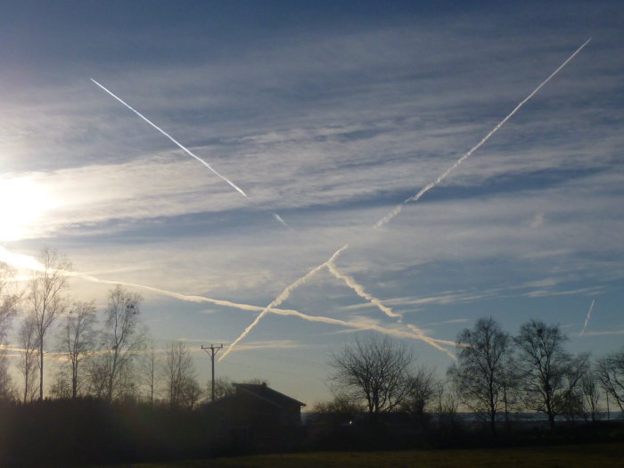 Himlavy med flera kondensstrimmor från flygplan ovanför ett landskap och hus.