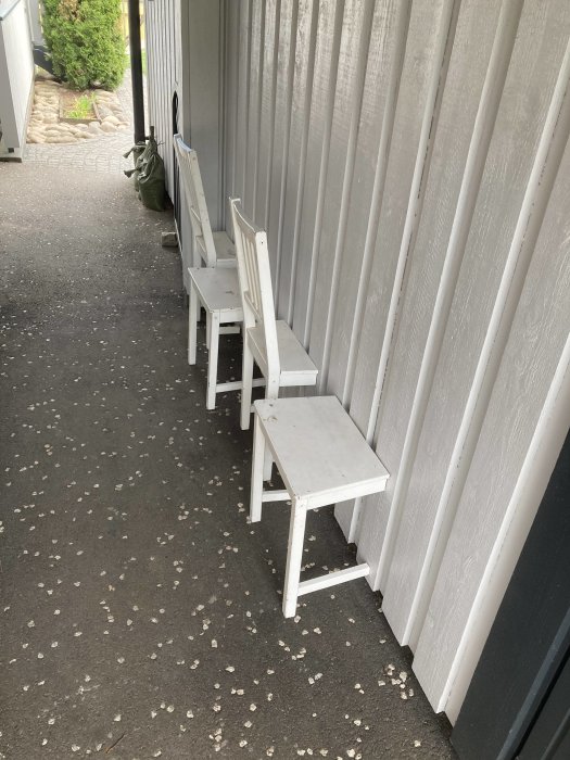 Två gamla trästolar, ommålade och slipade, står vid en husvägg redo att oljas och monteras.
