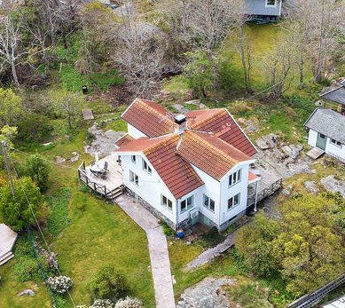 Flygbild över vitt, traditionellt hus från 1907 med rött tak på skärgårdsö.