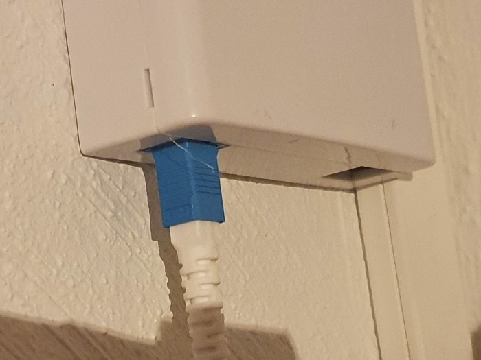 En vit fiberbox med en blå tejpad SC LC-kabel ansluten till underkanten.