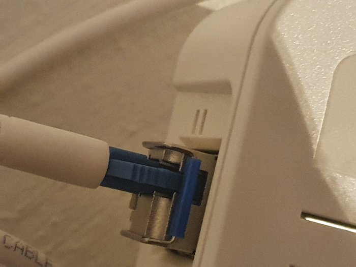 Optisk fiberkabel med blå SC-kontakt ansluten till en vit mediakonverter eller fiberbox.