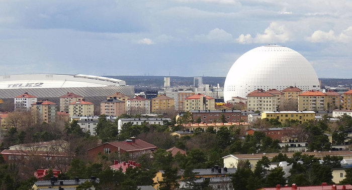 Vy över Globen, en känd kupolformad byggnad i Stockholm, med omgivande bebyggelse och Tele2 Arena i bakgrunden.