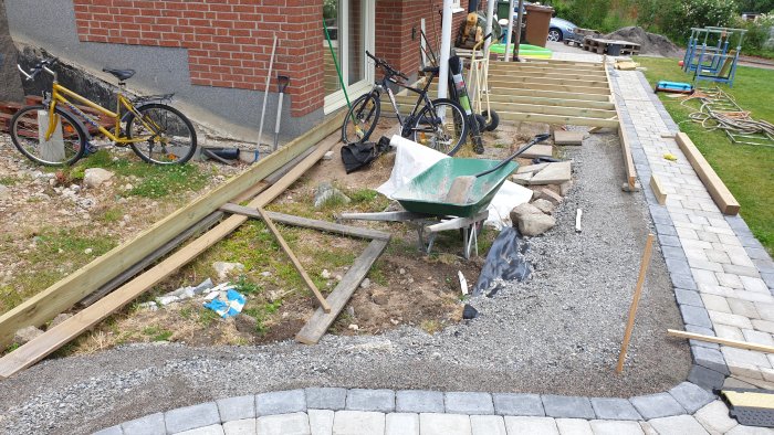 Byggplats med pågående arbete på altan längs kantsten och stenplattor, material och verktyg syns.