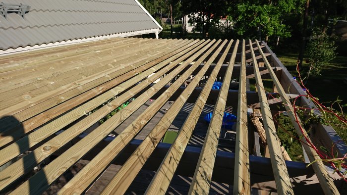 Nyinstallerat solskydd på pergola med diagonalt skurna träplankor och skruvar med cc120mm mellanrum i trädgårdsmiljö.