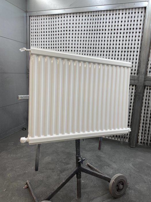 Nymålad radiator på stativ i målarverkstad med ommålad insida synlig.