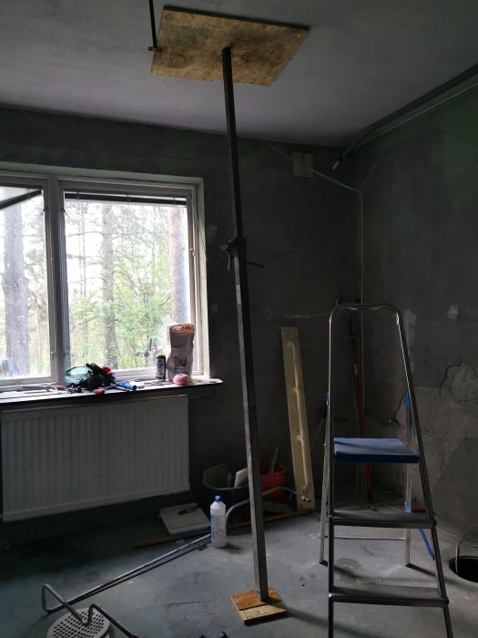 Ett rum under renovering med en stämp som håller upp en OSB-platta i taket, stege, och verktyg.