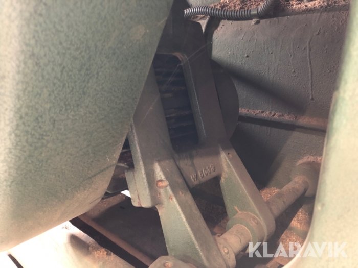 Närbild av delar i en maskin med fokus på en metallarm och kugghjul täckta av damm och smuts.
