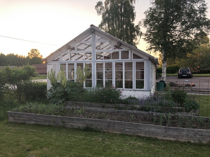 Södergavel i glas på hus med odlingsbädd framför, ackumulatortank och stuprör syns.