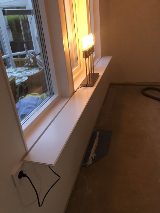 Nyinstallerad vit fönsterbräda med en bordslampa, framför ett fönster i ett rum under renovering.