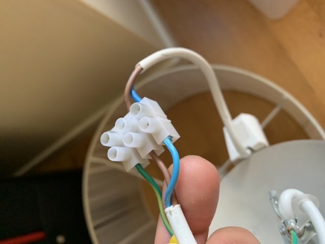 En hand håller en kopplare med flera ingångar, anslutna till en mix av blå, bruna och vita kablar.