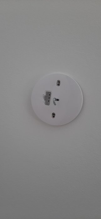 Jordat lamputtag på vit vägg med en öppen centralplatta och synliga ledningar.