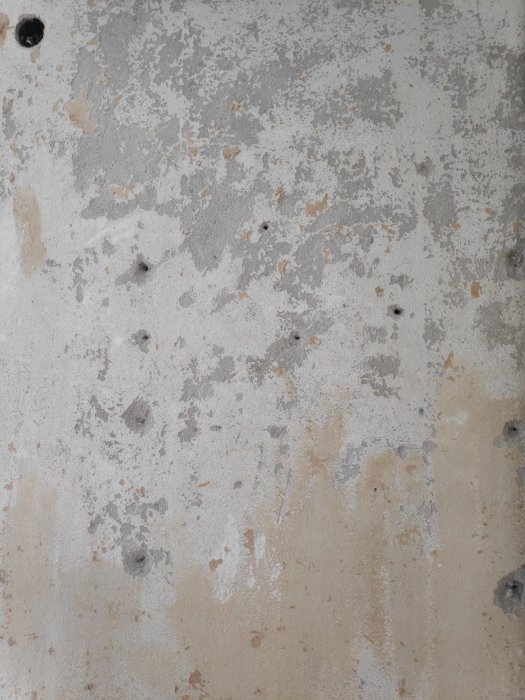 Naken lättbetongvägg med bortskrapade tapetlager, synliga hål och sprickor.