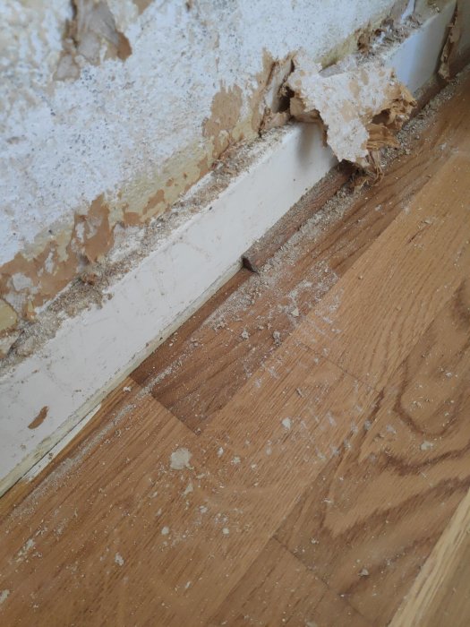 Skadad och sliten dörrlist i ett renoveringsprojekt med bortskrapad gammal tapet och parkettgolv.