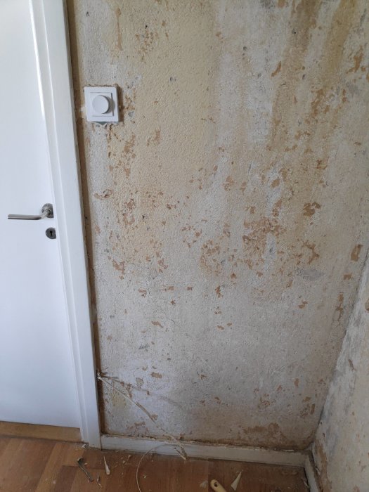 Vägg med skrapade tapetlager och synlig strömbrytare vid en dörrkant.