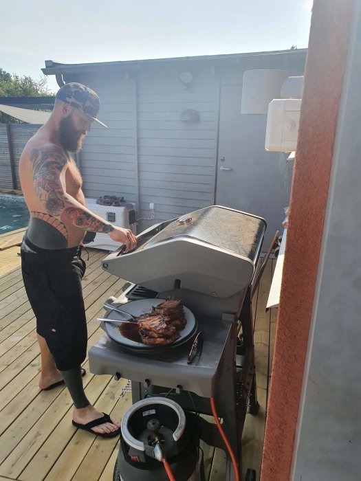 Man grillar kött på en gasolgrill under en solig midsommarafton.