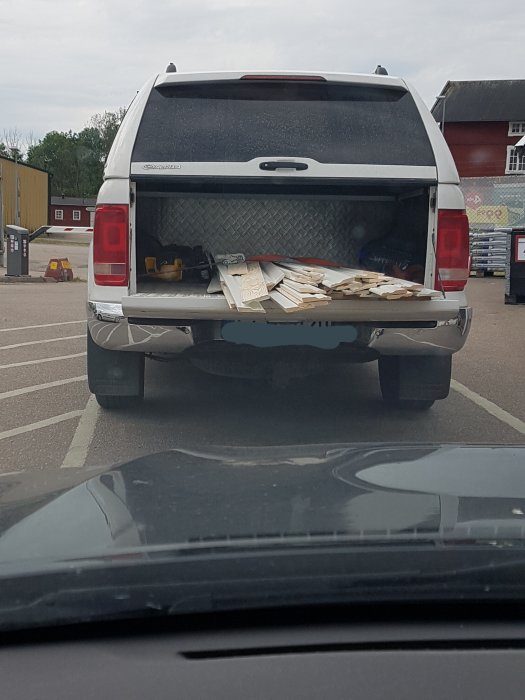 Lastbil med öppen bakdörr lastad med lösa träbitar på en parkeringsplats.