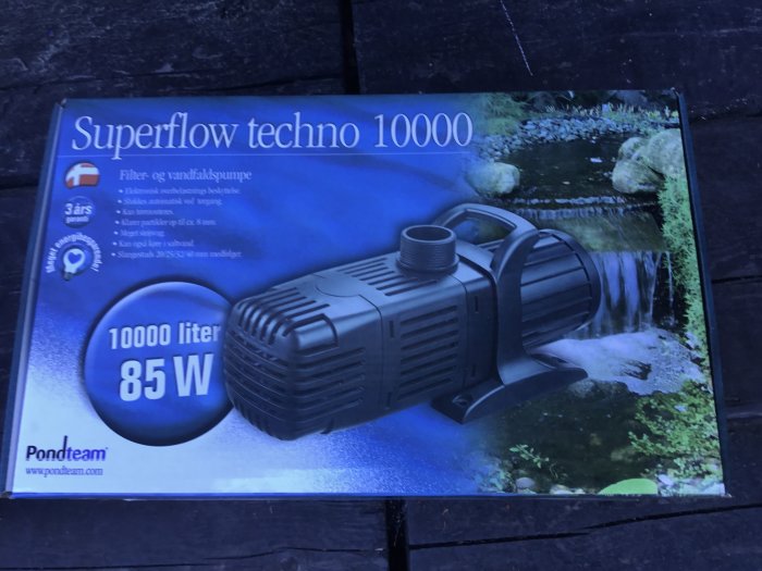 En vattenpump "Superflow techno 10000" på en förpackning med bild av en trädgårdsdamm och vattenfall.