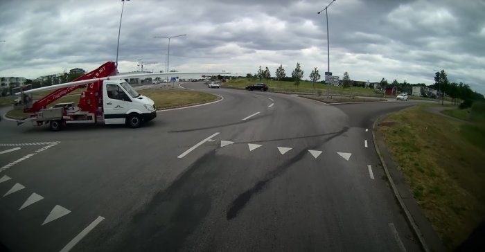 Röd kranbil från Frosings i en rondell tagen från en dashcam, molnig himmel i bakgrunden.