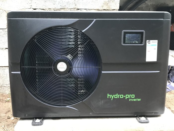 Svart Hydro-Pro inverter värmepump placerad mot en betongvägg.