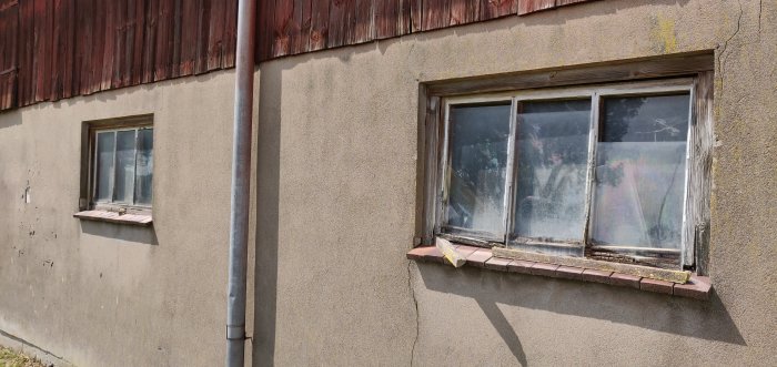 Nedgången ladugårdsfasad med slitet tegeltak, spruckna fönsterkarmar och avskalad färg.