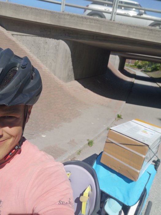 Person med cykelhjälm tar selfie med en cykelvagn lastad med paket.