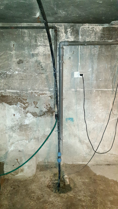Dräneringspump och avloppsrör i äldre källare, slang går mot krypgrund.