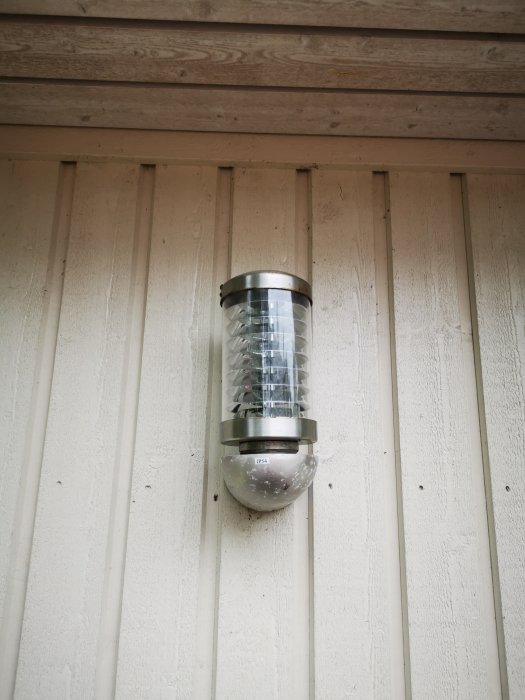 Utomhuslampa fäst på en vit trävägg med vertikala paneler, avsedd för installation av smarta belysningssystem.
