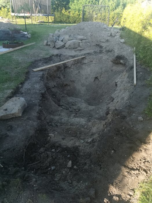 Uppgrävd trädgårdsdamm på villatomt med synlig sten och krossmaterial, nära färdigställd.