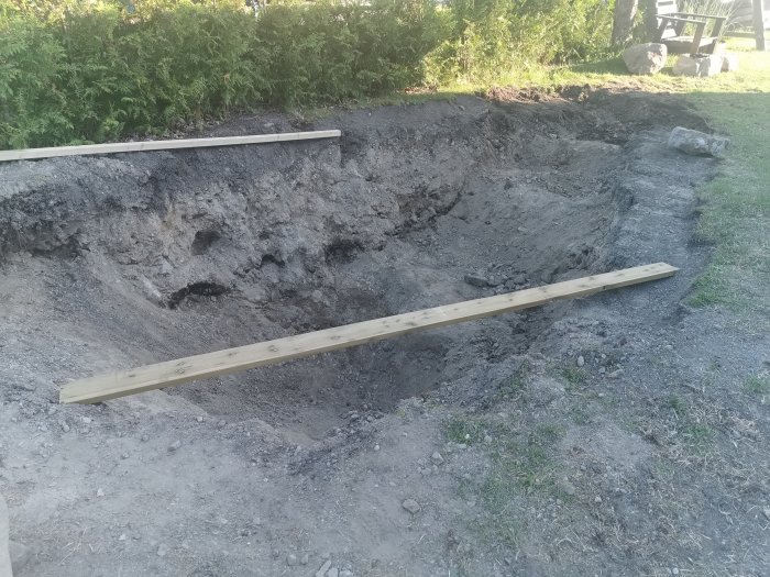 Grävd trädgårdsdamm på villatomt med synliga stenar och krossmaterial längs kanterna.